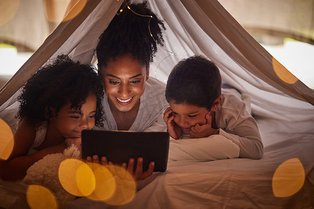 睡前故事摄影照片_家庭、平板电脑和在线流媒体与孩子一起观看睡前故事、电影或动画片，在毛毯堡垒中享受教育乐趣。