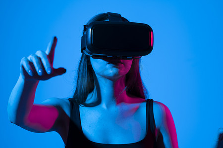 虚拟现实现实摄影照片_身穿黑色 T 恤的快乐黑发女孩惊讶地使用虚拟现实 VR 耳机眼镜获得体验，并探索新的网络世界。