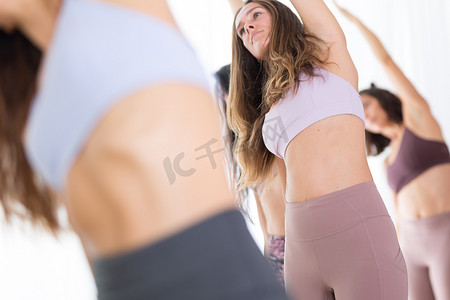 一群年轻的运动美女在瑜伽馆里，与教练一起练习瑜伽课，以半月体式站在一起。