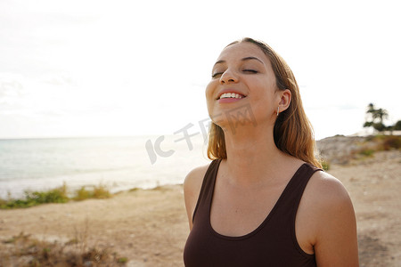 呼吸新鲜空气摄影照片_在沙滩上呼吸新鲜空气的轻松快乐的年轻女人