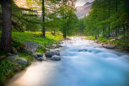 莫兰迪几何色块摄影照片_春天飘渺的河流和高山草甸，意大利大帕拉迪索阿尔卑斯山