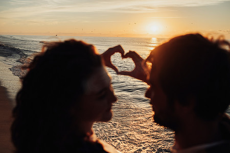 在风景秀丽的日出背景下，男人和女人用手指表达心意，年轻夫妇在海边迎接黎明