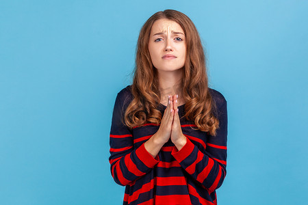 穿着条纹休闲风格毛衣的女人手牵着手祈祷，用恳求的表情看着，乞求帮助，请求宽恕。