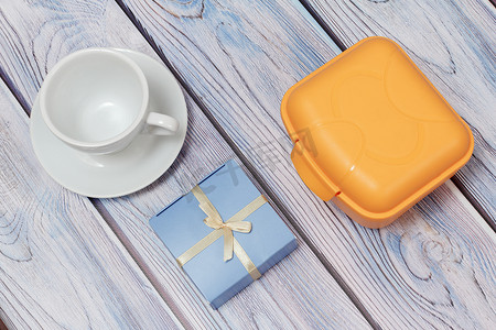 塑料黄色午餐盒、礼品和带碟子的杯子在木制背景上。