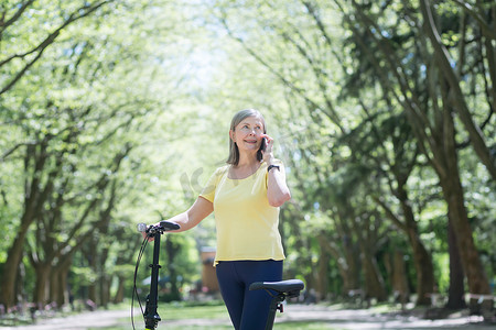 在夏日公园散步的高级快乐女人，微笑着，骑着自行车打电话聊天