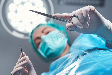 在手术室明亮的灯光下，身着医疗制服的女性外科医生从下方使用专业工具