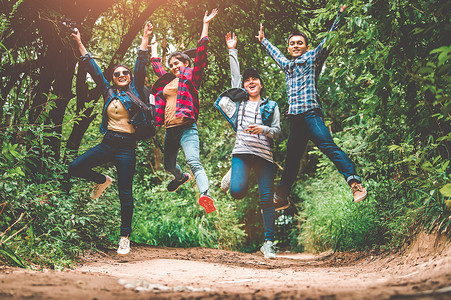 一群快乐的亚洲青少年冒险旅行者在户外森林背景的山上一起跳跃。