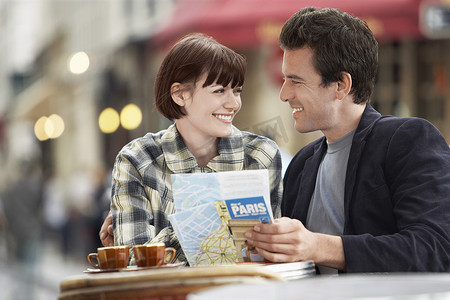 快乐的年轻夫妇在户外咖啡馆拿着旅游指南