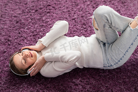 一个小女孩仰面躺在地毯上，用耳机听音乐。