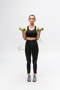 哑铃摄影照片_白色背景的白人妇女的肖像，身穿黑色健身服，用哑铃锻炼。
