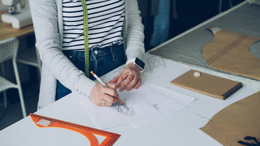 创意服装设计师专注于用铅笔在纸上绘制女装草图。