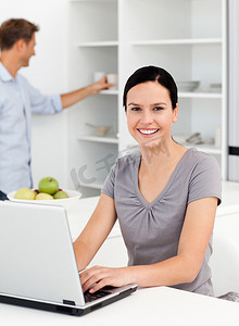 快乐的女人和男友在厨房里用笔记本电脑工作