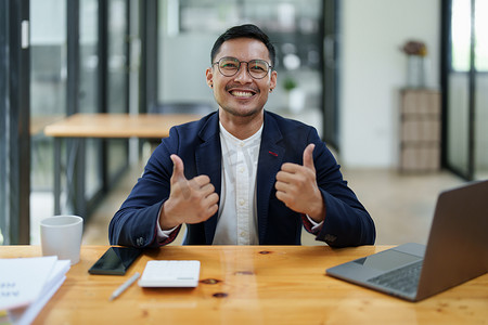 一位亚洲男性企业主站在电脑前的肖像，在成功投资后表现出幸福感