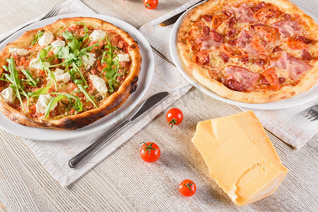 圆火腿摄影照片_浅色木桌上的白色圆盘上有三文鱼、羊奶酪、香肠、火腿、萨拉米香肠和酱汁、西红柿的披萨。
