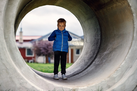 一个可爱的小男孩，穿着蓝色背心，站在一个巨大的混凝土隧道里。