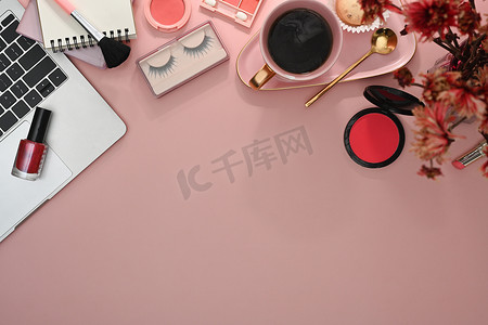 化妆小工具摄影照片_带笔记本电脑、化妆刷和粉红色背景化妆品的女性工作区。