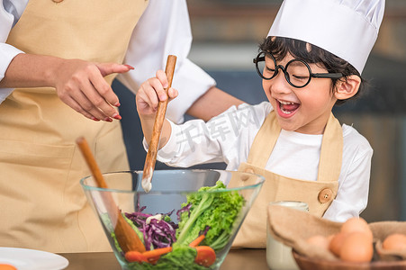 亚洲食物摄影照片_可爱的亚洲小快乐男孩对与有趣的母亲在家庭厨房做饭感兴趣。