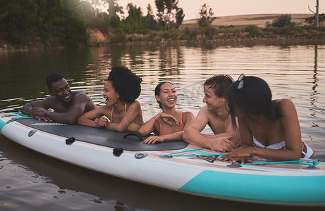 哈哈大笑卡通人物摄影照片_朋友们，度假，靠着桨板在湖里聊天，享受乐趣。