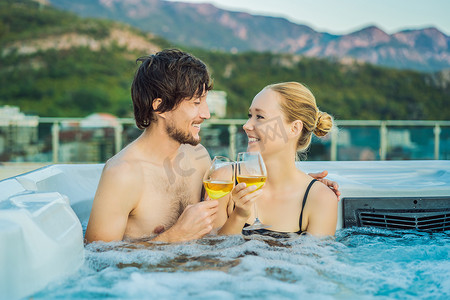 浴缸背景摄影照片_在绿色大山的背景下，享受快乐旅行时光假期生活的年轻无忧无虑的快乐微笑夫妇在热水浴缸中放松的肖像