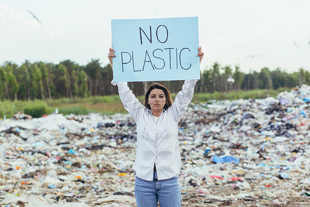 女志愿者在垃圾填埋场举着无塑料海报，积极分子与环境污染作斗争