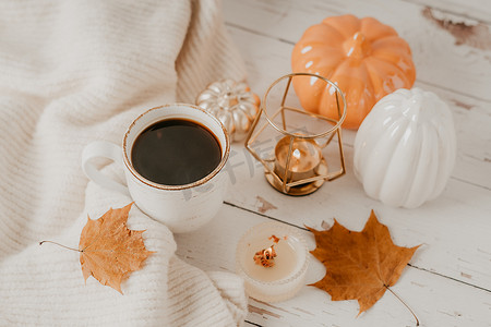 静物细节、一杯茶或咖啡、南瓜、蜡烛、白桌背景上有叶子的早午餐、舒适房子里的家居装饰。