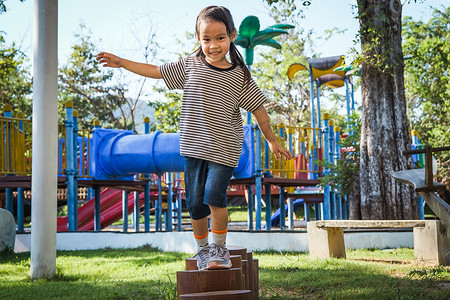 平衡木摄影照片_活跃的小女孩在公园的室外操场上走在平衡木上。