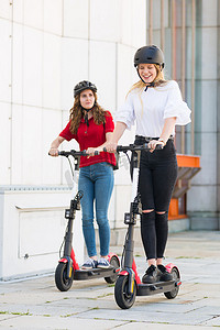 公共生活摄影照片_在城市环境中骑着公共租赁电动滑板车的时髦时髦的少女。