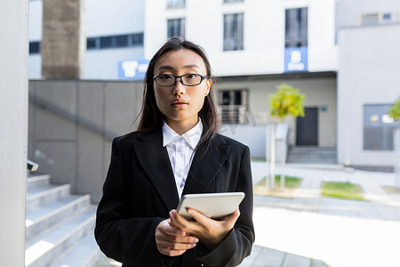 商务正装摄影照片_身穿商务正装的亚洲女商人站着，手里拿着平板电脑工作