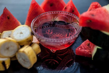 香蕉和西瓜摄影照片_玻璃碗中木质表面的西瓜面膜或面膜，以及由西瓜和香蕉切成三角形的西瓜片。用于瞬间自然发光。