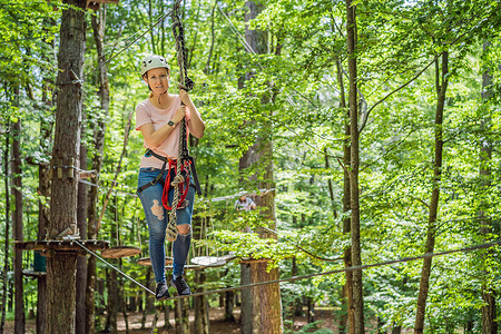 滑索摄影照片_快乐的女女孩在森林中的极限公路电车滑索中滑翔攀爬，在树上的登山扣安全链接上到树顶绳索冒险公园。