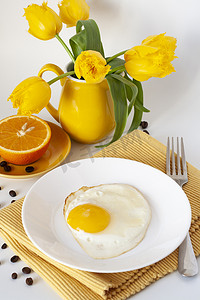 郁金香花束摄影照片_明亮的早餐：鸡蛋、多汁的橙子、黄色郁金香花束、黄色餐巾和叉子。