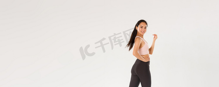 时髦苗条的黑发亚洲女孩的全长侧面肖像正在健身，在健身房锻炼，带着积极和坚定的表情行走，拥有体育中心的会员资格