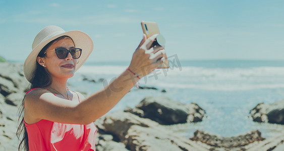 戴帽子的女人在海上拍照，拉丁女孩在度假拍照，女孩在沙滩上自拍的后视