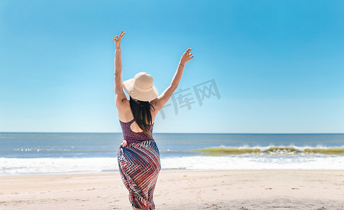 海滩上戴着帽子的女人，年轻女人在海滩上举起双手