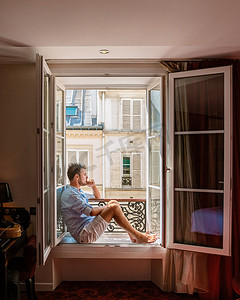 年轻人坐在窗前，眺望巴黎这座城市。