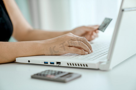 女人坐在笔记本电脑前网上购物，手里拿着银行卡，特写