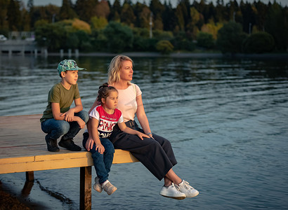日落时分，妈妈带着孩子坐在池塘边的码头上。