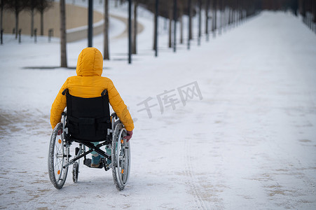 残障人士康复摄影照片_冬天，白人残疾妇女坐在公园的椅子上。