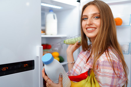 一位年轻金发女子从冰箱里拿食物的画像