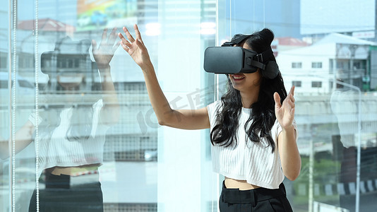 界面交互摄影照片_兴奋的女员工戴着虚拟现实眼镜，在现代办公室与数字界面交互。