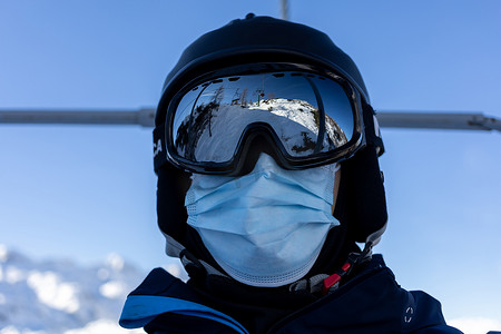 滑雪胜地男子戴着头盔和医用面罩乘坐缆车