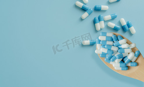 在木勺和蓝色背景上的蓝白色抗生素胶囊丸的顶部视图。