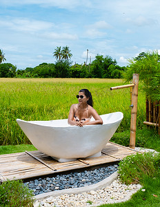 在泰国一家寄宿家庭度假时，妇女们在浴缸里洗澡，那里有绿色的稻田
