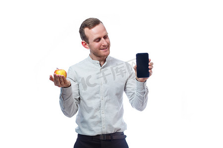 苹果手机黑色手机摄影照片_白人男性商人手持黑色手机，手里拿着一个红黄色的苹果。