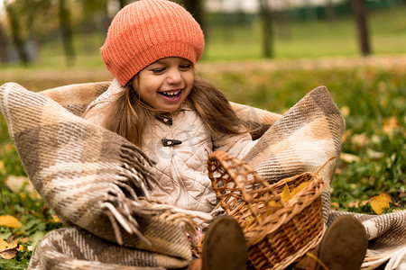 好的看的背景摄影照片_穿着橙色贝雷帽的小可爱学龄前未成年女孩在黄色落叶篮子的格子上笑得很好微笑看着相机在秋天公园的寒冷天气。