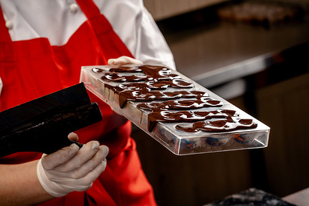 一位身穿红色制服、戴着白色无菌手套的女糖果师在桌子上用牛奶巧克力制作了一套彩色巧克力。