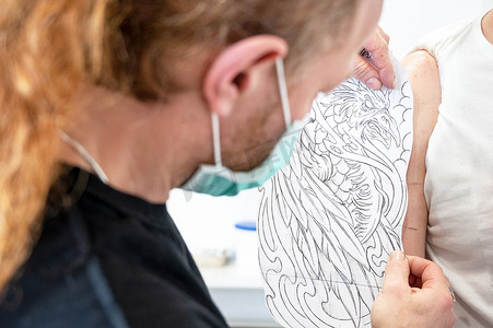 熟练的纹身艺术家把素描放在一个人的手臂上。
