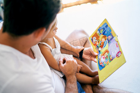 爸爸在床上给小女孩读一本童话书
