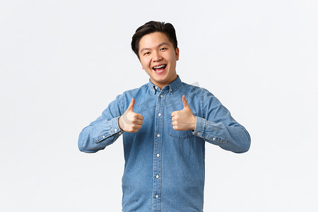 满意快乐的亚洲男人戴着牙套，竖起大拇指表示赞同，喜欢并推荐产品或服务，祝贺朋友取得成就，说做得好，优秀，白色背景