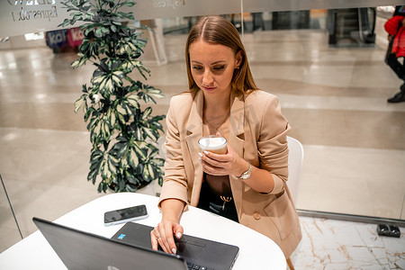 一位女商人坐在咖啡馆里，在电脑前工作，喝着咖啡。